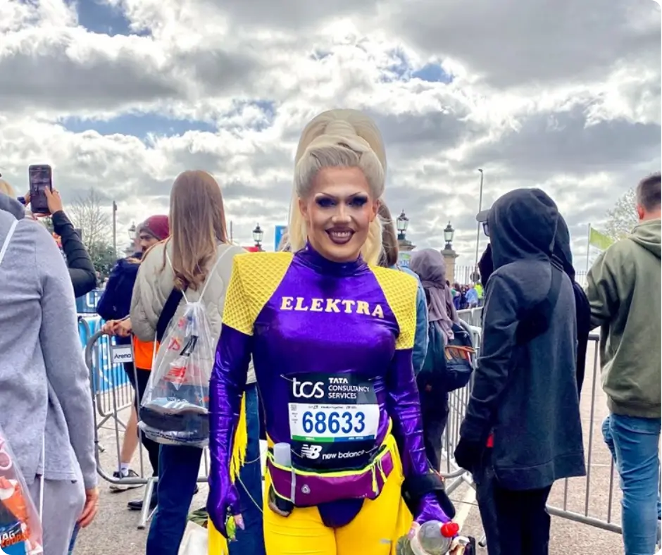 Image of Ru Paul's Drag Race star Elektra Fence at the London Marathon in full drag, bright purple and yellow clothing with "Elektra" across the front of the chest.