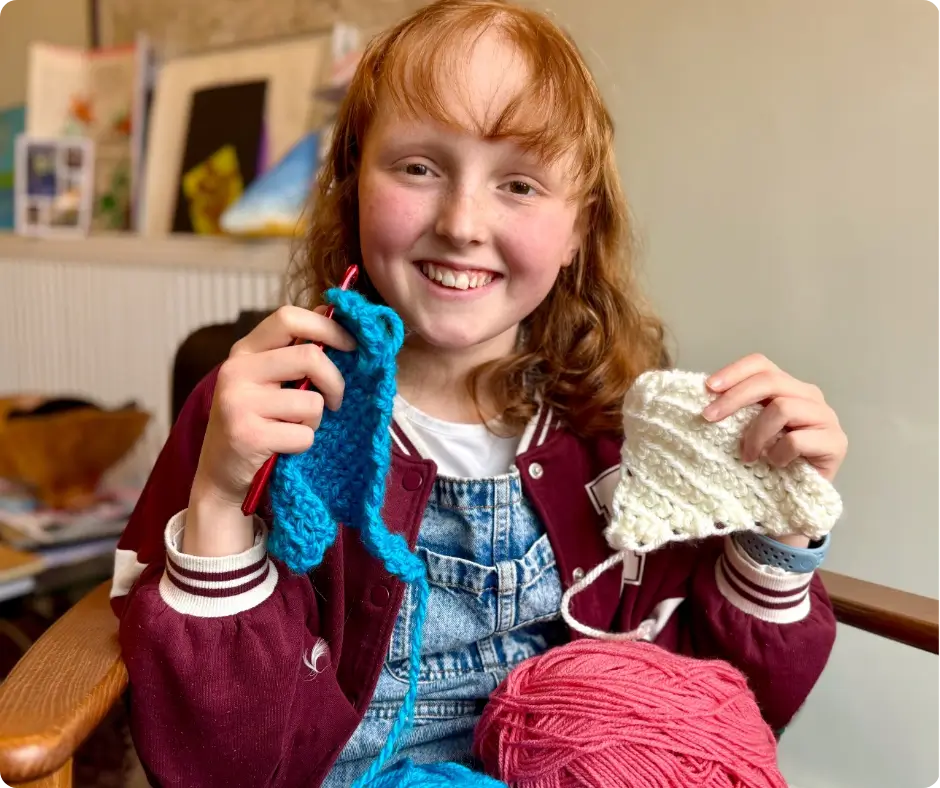 Image of Kirsty smiling and holding two of the bunting triangles she crocheted during her 70-week chemotherapy treatment plan.